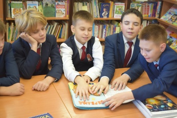 Четверо школьников в форме рассматривают иллюстрированную книгу.